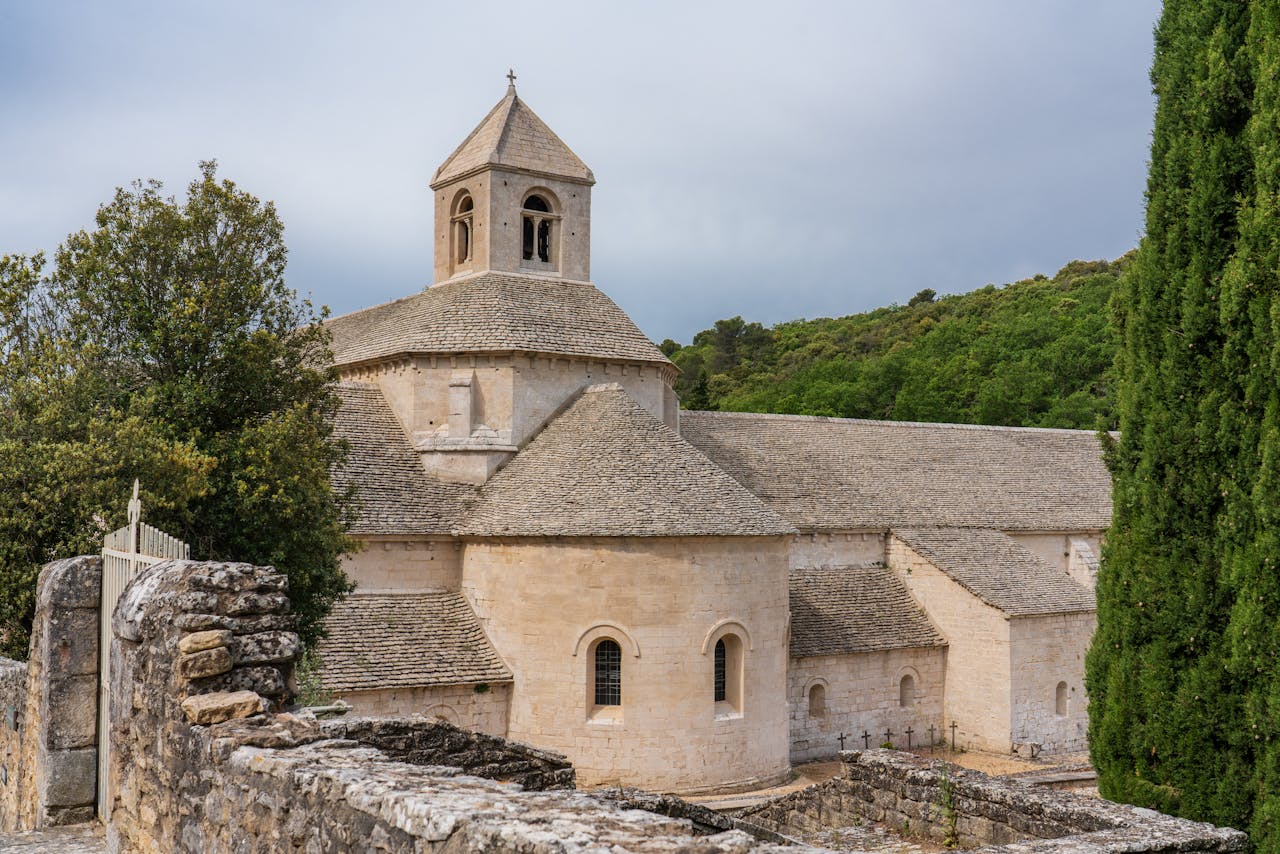 Stone-built chapel amidst lush greenery under a cloudy sky, showcasing ancient architecture.